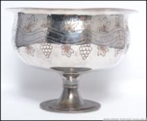 A silver plated on copper pedestal bowl being decorated with grapes and vines in a continuous