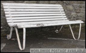 A Victorian cast iron garden bench with sloping seat and back with wooden slats being painted white