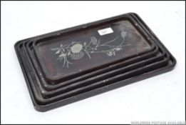 A 20th century stack of graduating Chinese trays of wooden laquered form inlaid to each with white