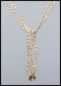 A triple string cultured rice pearl necklace with stylised pearl set yellow metal clip clasp