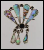 An white metal brooch with inset abalone shell and black enamel in the shape of a peacocks tail