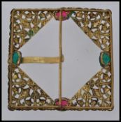 A early 20th century large yellow metal belt buckle set with green and red stones and Fleur de Lys