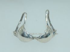 A white metal brooch - tests silver - fashioned in the shape of a bikini bra top with c clasp .