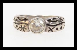 A contemporary 925 silver band ring with bezel set clear stone with symbol decoration to shoulders.