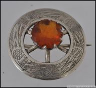 A white metal scottish thistle brooch with central orange stone with etched thistle decoration and