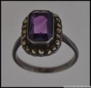 A white metal dress ring set with a central emerald cut amethyst stone surrounded by a halo of