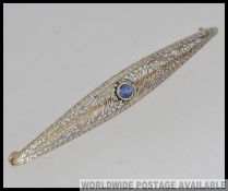 A 14ct gold and silver filigree bar brooch with inset blue round cut sapphire. Stamped 14k.