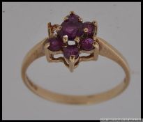 A 9ct hallmarked ring with pink red gem stones in a daisy setting.one stone missing. Weight 1.8g.