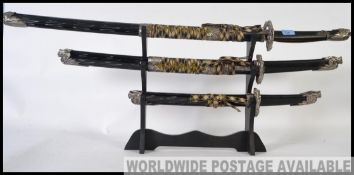 A trio of graduating replica Japanese Bushido style Samurai swords with ebonised sheaths and white