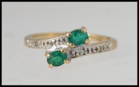 A 9ct gold cross over ring set with two oval cut emeralds and illusion set diamonds.