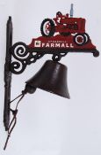 A cast iron exterior hanging door bell on a bracket, the top decorated with a Farmall tractor.