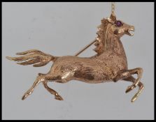 A stunning 9ct gold brooch in the form of a running horse having garnet stone eyes complete with