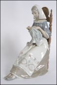 A large Lladro figurine of a seated lady sewing a tapestry.