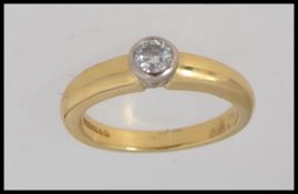 An 18ct gold ring set with central round cut solitaire diamond in a rub over setting.