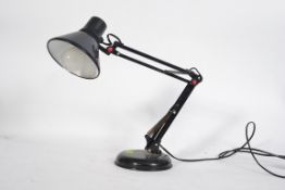 A retro black anglepoise style lamp, raised on a circular base with a conical shade.