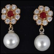 A cased pair of ladies freshwater pearl and cz adorned earrings having inset garnet stone centres.