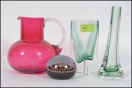 A collection of glass items to include a handmade cranberry jug, paper weight and glass vases,