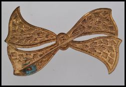 A 1920s vintage gold tone brooch in the shape of a bow with embossed foliate decoration.