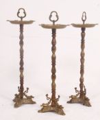 A collection of 3 early 20th century brass rococo floorstanding ashtrays having twin tiers and