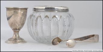 A silver hallmarked egg cup together with a pair of silver sugar tongs and a cut glass and silver