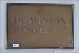 A mid century brass wall mounted advertising business plaque for Dominion Insurance set to a wooden