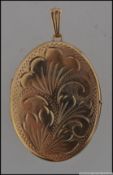 A large hallmarked 9ct gold locket pendant with scroll decoration to front and scalloped bale.