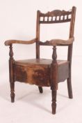 A Victorian commode chair in oak being raised on turned legs having a hinged seat with decorative