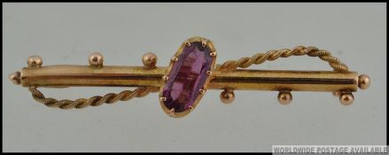 An 18ct gold bar brooch with central oval cut amethyst in a claw setting with rope twist swag and