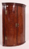 A 19th century Georgian bow front corner cabinet having twin doors with flared cornice,