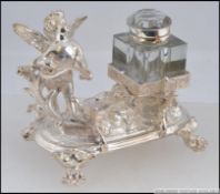 A silver plated desk set, having a pen holder in the form of a cherub playing a string instrument,