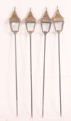 A collection of four contemporary brass garden lanterns, each raised on a tall brass ground spike,
