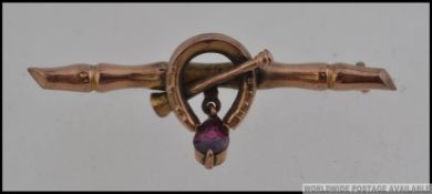 A Victorian 9ct gold sweetheart bar brooch with lucky horse shoe and hunting horn with amethyst