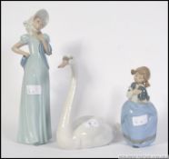 A boxed Lladro swan figurine together with 2 boxed Nao figurines, one of a child, the other a dame.