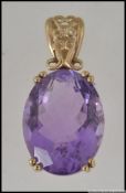 A large hallmarked 9ct gold pendant set with an oval cut amethyst in a prong setting with scroll