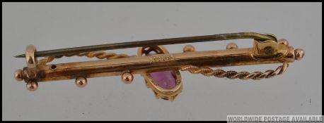An 18ct gold bar brooch with central oval cut amethyst in a claw setting with rope twist swag and