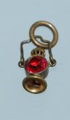 An early 20th century yellow metal carriage lamp lantern charm set with a red paste stone .