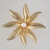 A vintage Sarah Coventry gold tone flower brooch with central pearl and roller clip clasp.