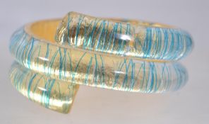 A vintage heavy lucite wrap around bangle with encased layered metal leaf and blue metallic strands.