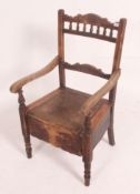 A Victorian commode chair in oak being raised on turned legs having a hinged seat with decorative
