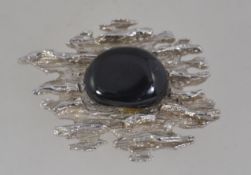 A large vintage brutalist textured white metal brooch with central black glass stone with roller