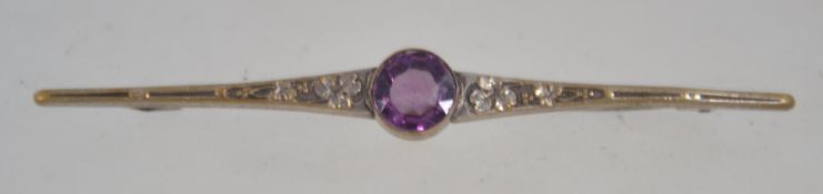 An Edwardian bar brooch set with a purple stone decorated with foliate shoulders. Measures 8.5cms.