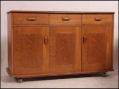 A 1970's retro Ercol style sideboard raised on ball castors with thin plinth having metamorphic