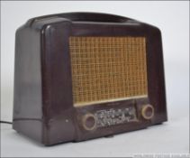 A vintage bakelite valve radio having a brown casing dials and display to the front with a mesh