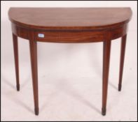 A Georgian mahogany inlaid demi - lune card table / games table being raised on square tapered legs