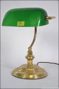 A 20th century bankers desk lamp having a green glass shade being raised on a brass stand with.