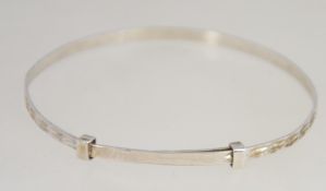 A silver childs christening bracelet of expanding form with chase decoration being stamped Silver.