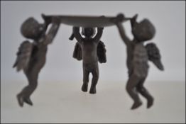 A bronze candle stand being supported by three winged cherubs H5cm