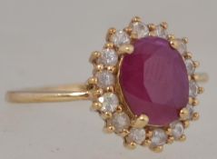 A 9ct gold ruby and diamond cluster ring. The central oval ruby with diamond surround.