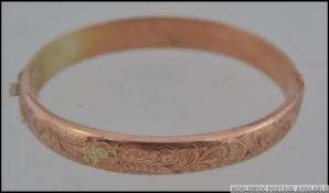 A hallmarked 9ct gold bangle bracelet with foliate scroll decoration with clip and safety clasp.