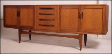 A 1970's G-Plan teak sideboard of low and wide form raised on turned legs with a series of